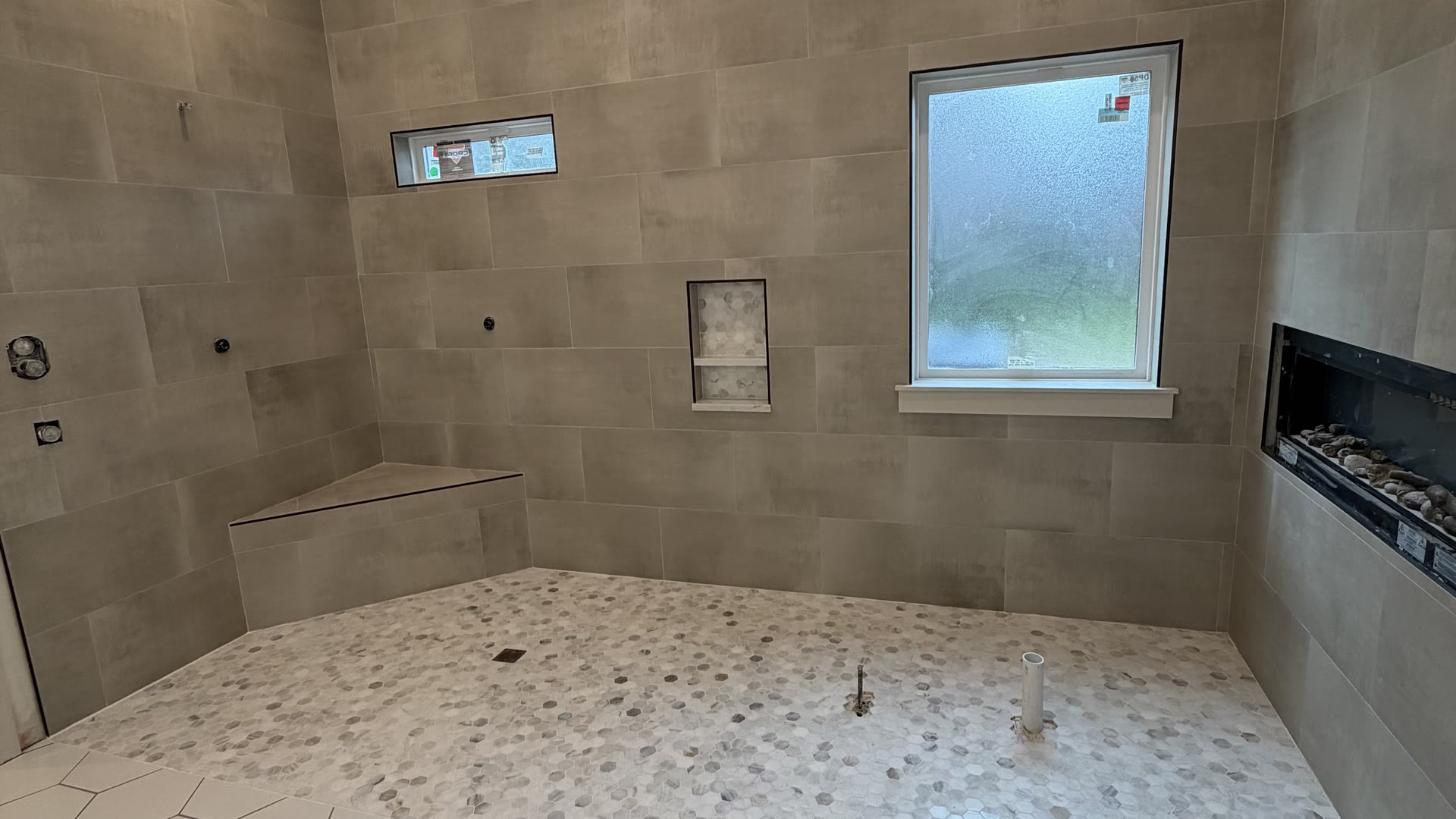 Master bath with a linear fireplace, large-format wall tile and a white hex floor