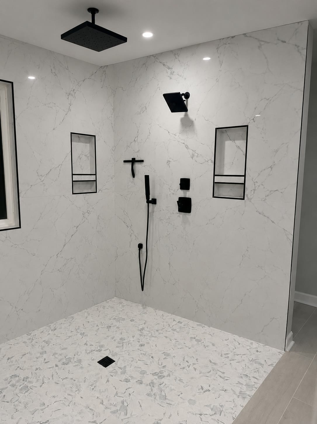 Finished walk-in shower in large-format marble-look porcelain with black fixtures and black-trimmed niches